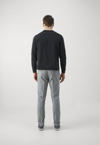 Svart lättviktsjacka med långa ärmar och rund halsringning, kombinerad med grå skräddarsydda byxor och avslappnade sneakers. Enkel, modern snitt.