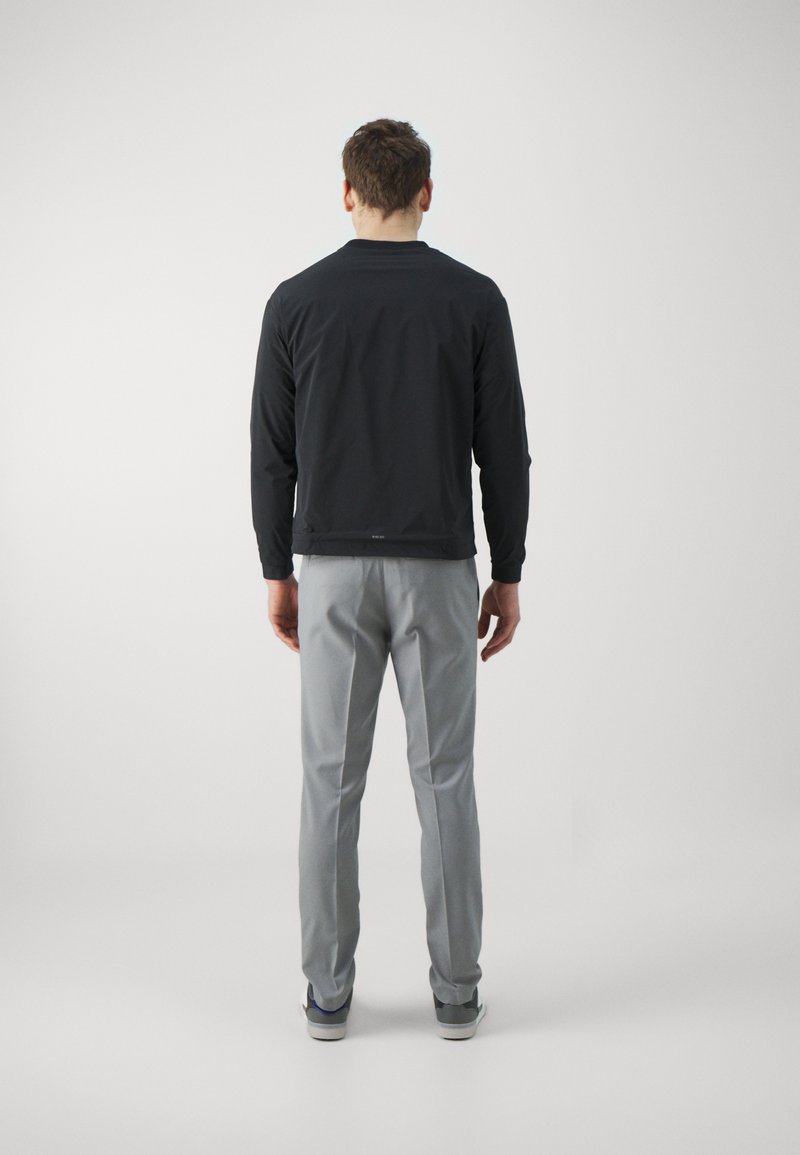 Schwarze, leichte Jacke mit langen Ärmeln und Rundhalsausschnitt, kombiniert mit grauen, maßgeschneiderten Hosen und lässigen Sneakern. Schlichte, moderne Schnittführung.