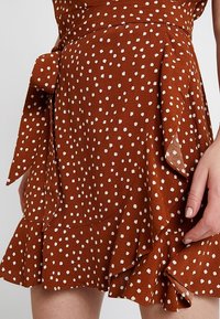 Jupe en tissu léger à pois marron, avec un ourlet volanté et un détail de lien à la taille, ornée de petits pois blancs.