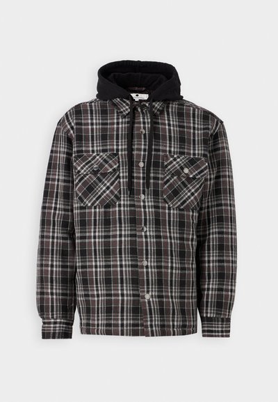 Chemise overshirt en flanelle à carreaux noirs avec deux poches poitrine, rayures grises et blanches, et une capuche noire. Elle comporte des fermetures à boutons et un tissu résistant.