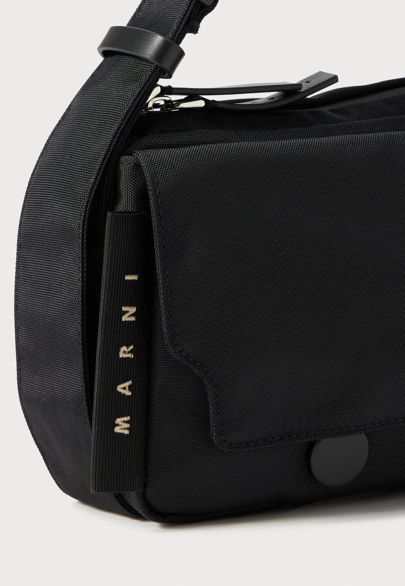 Sac bandoulière noir avec une sangle ajustable, poche à rabat à l'avant, détail en zip et étiquette en tissu avec le lettrage "MARNI" sur le côté.