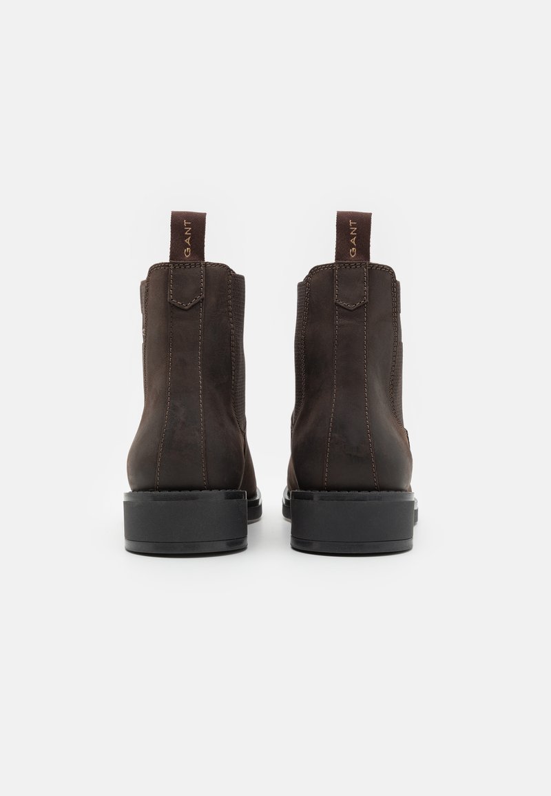 Ein Paar dunkelbraune Lederstiefel mit schwarzem Sohlen und Zuglaschen, die mit "GANT" beschriftet sind, von hinten auf einem weißen Hintergrund gezeigt.