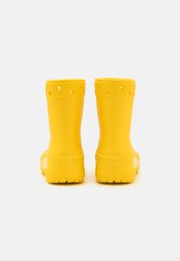 Une paire de bottes en caoutchouc imperméables et jaunes vives vues de l'arrière, avec des poignets texturés et des trous de ventilation près du haut.