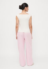 Top senza maniche color crema con scollatura ampia, abbinato a pantaloni larghi rosa chiaro. Il tessuto appare morbido con una delicata texture.