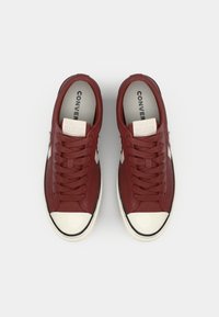 Red leather sneakers with white rubber toe cap, black outsole, and matching laces. "Converse All Star" branding inside.