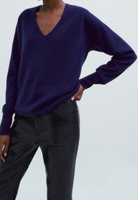 Navy blue v-neck sweater in soft knit fabric with long sleeves, paired with fitted black leather pants featuring a side pocket detail.