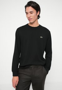 Μαύρο μακρυμάνικο πουκάμισο από βαμβάκι, με στρογγυλή λαιμόκοψη και μικρό πράσινο λογότυπο Lacoste στο στήθος. Λεπτή υφή και εφαρμοστό σχέδιο.