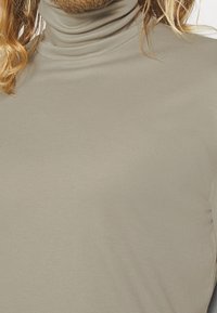 Maglione beige a collo alto in un tessuto morbido e liscio, con un design aderente e una sottile costina attorno al collo. Vista ravvicinata.