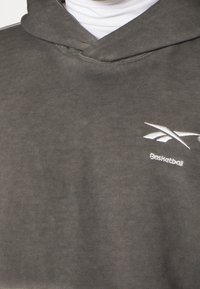 Felpa grigia con cappuccio in tessuto morbido, caratterizzata da un logo bianco e la scritta "Basketball" sul lato sinistro. Vestibilità classica e rilassata.