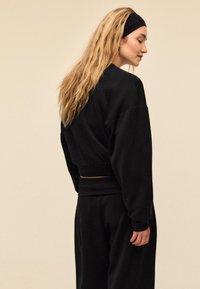 Schwarzer Sweatshirt mit lässiger Passform, gerippten Bündchen und einem Bund. Die Haare sind wellig gestylt. Einfaches Design ohne Muster oder Verzierungen.