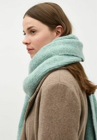 Sosete tricotate de culoare albastru deschis, cu o textură moale, înfășurate în jurul gâtului, asociate cu o haină din lână maro. Design simplu și minimalist.