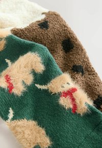 Manta de punto que presenta tres secciones: crema, marrón con manchas negras y verde con figuras beige difusas y acentos rojos. Textura suave.