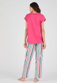 Haut rose à manches courtes avec un col rond associé à un pantalon ample rayé dans des tons de blanc, vert, rouge, orange et bleu.