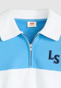 Polo en azul claro y blanco, con cuello con cremallera, tejido texturizado y bordado en azul marino con las letras "LS" en el pecho.