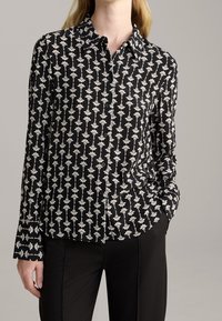 Black button-up shirt with a white floral pattern, long sleeves, and a collar. Smooth fabric with a fitted design. Paired with black pants.