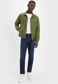 Oliwkowa, zapinana na guziki kurtka z dwoma przednimi kieszeniami, noszona na białej koszulce. Połączona z niebieskimi dżinsami i białymi trampkami.