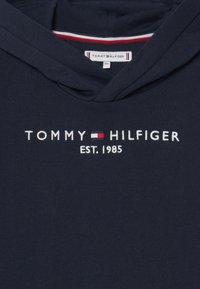 Námořnická modrá mikina s kapucí vyrobená z bavlny, s bílým vyšitým logem "TOMMY HILFIGER EST. 1985" a červenobílým pruhovaným výstřihem.