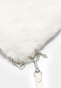 Bijela clutch torbica od umjetnog krzna s srebrnim metalnim detaljima, koja ima zatvaranje na patentni zatvarač i odvojivu naramenicu. Mekana tekstura i kompaktan oblik.