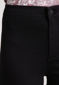 Jeans de mezclilla negra con una textura suave, que cuentan con un cierre de botón y costuras contrastantes en la cinturilla y las costuras laterales.
