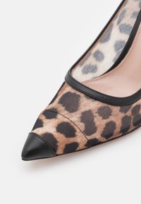 Chaussure à talon haut à bout pointu en tissu imprimé léopard avec garniture en cuir noir sur le bout et l'ouverture.