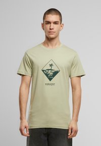 Camiseta de algodón verde claro con un gráfico de diamante que incluye una palmera y olas, impreso en verde oscuro. Diseño de mangas cortas y cuello redondo.