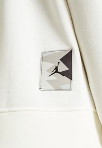 Il tessuto del sudario bianco presenta un'etichetta rettangolare con un design geometrico grigio e nero e il silhouette nera di una figura che salta.