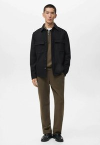 Black button-up shirt with two chest pockets, olive green polo underneath, brown pants, and black shoes. Simple, modern design and textures.
