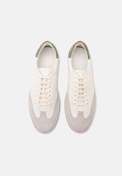 Paire de baskets décontractées en cuir blanc et gris clair avec lacets et colliers de talon verts rembourrés sur un fond clair uni.