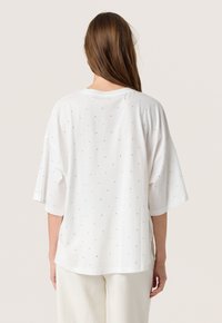 Hvid oversized t-shirt med korte ærmer, der har et tekstureret prikket mønster og en rund halsudskæring, som viser en afslappet pasform.