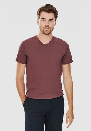 T-shirt z dekoltem w serek i krótkim rękawem w burgundowym kolorze, o miękkiej teksturze. Noszony z ciemnymi spodniami, charakteryzuje się prostym wzornictwem i luźnym krojem.