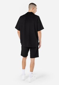 Maglietta nera a maniche corte in tessuto testurizzato, abbinata a pantaloni corti coordinati. Indossata con sneakers bianche e calze corte.