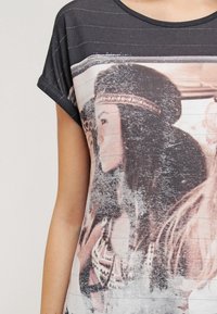 Czarna koszulka z krótkim rękawem z wyblakłym nadrukiem przedstawiającym kobietę, z poziomymi paskami i miękkim, teksturowanym materiałem.
