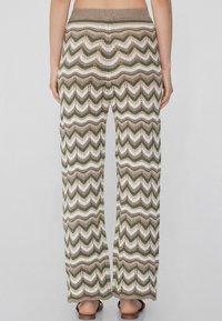 Gehaakte wijde broek met een zigzagpatroon in groen, bruin en wit. Elastische tailleband en opengehaakte textuur door de broek.