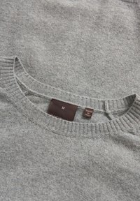 Grauer Pullover mit rundem Ausschnitt und gerippten Bündchen. Verfügt über ein Etikett mit der Größe "M" und "Hergestellt in Italien" auf der Innenseite. Weiche Textur.