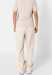 Beige katoenen t-shirt en broek met wijde pijpen, met een achterzak, een relaxte pasvorm en een zacht gestructureerde stof, van achteraf bekeken.