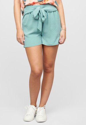 Helle türkisfarbene Shorts aus strukturiertem Stoff, mit einem elastischen Taillenbund und einem gebundenen Gürtelakzent. Kombiniert mit weißen Sneakers.
