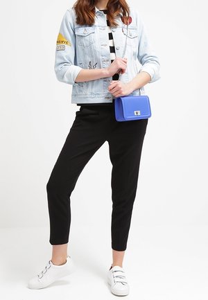 Ljusblå denimjacka med lappar, svarta tajta byxor och vita sneakers. En blå axelremsväska förstärker den avslappnade stilen.
