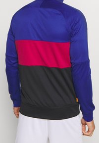 Pullover made of lightweight fabric featuring a color-block design with blue, red, and black sections. Smooth texture with ribbed cuffs.