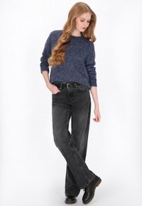 Blauwe, textuurgehaakte trui gecombineerd met zwarte high-waisted denim jeans en zwarte veterschoenen, wat een ontspannen silhouet creëert.