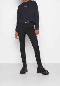 Černé krátké tričko s dlouhým rukávem a červenou nášivkou, doplněné černými úzkými cargo kalhotami a černými platformními botami s tlustou podrážkou.