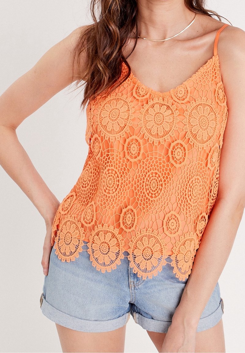Débardeur en crochet orange avec un motif de dentelle florale, des bretelles spaghetti réglables et un ourlet festonné, associé à un short en denim clair.