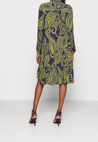 Grön och marinblå mönstrad klänning med långa ärmar, en lager-på-lager nederdel och en lös passform, tillverkad av lättviktig textil. Utsmyckad med ett paisleymönster.