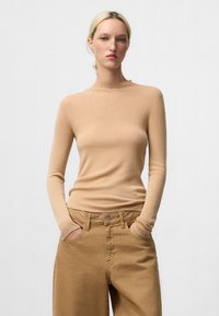 Haut beige clair à manches longues avec un col montant, fabriqué à partir d'un tissu lisse ; associé à un pantalon large beige. Design minimal, sans motifs visibles.
