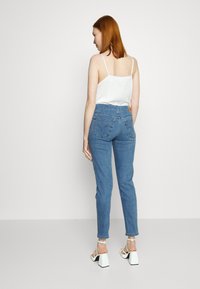Jeans din denim albastru cu talie înaltă și croială dreaptă, având două buzunare pe spate și o mică etichetă a brandului. Completate cu un top alb fără mâneci și sandale cu toc bloc.