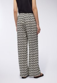 Pantaloni a gamba larga in un motivo floreale bianco e nero, realizzati in un tessuto leggero con una vestibilità ampia. Accentati da una vita liscia.