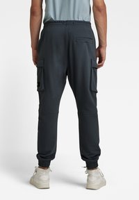 Pantalones de chándal gris oscuro con cintura elástica, puños acanalados y dos bolsillos laterales tipo cargo. Fabricados en un tejido suave, cuentan con un bolsillo trasero.