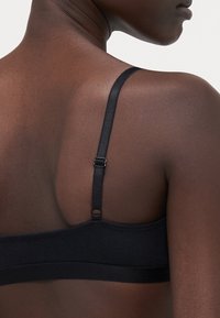 Svart BH laget av ribbet stoff, med justerbare stropper og et minimalistisk design. Bak har den en krok-og-øyelukking.