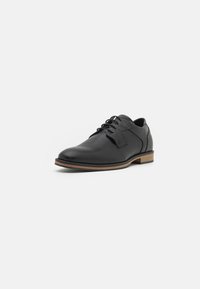 Scarpa in pelle nera con finitura liscia, design con lacci, punta arrotondata e suola marrone a contrasto; presenta dettagli testurizzati sulla linguetta.
