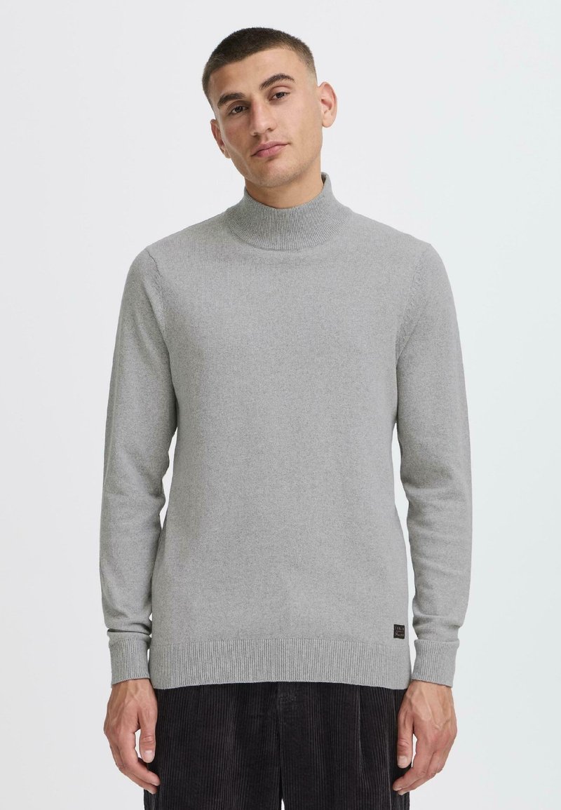 Maglione grigio a collo alto realizzato in tessuto a maglia fine, con maniche lunghe, polsini e orlo a costine, e una piccola etichetta con logo in fondo.