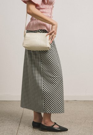 Mujer con blusa rosa, falda a cuadros en blanco y negro, zapatos planos negros, sosteniendo un bolso crema texturizado a su lado.